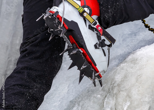Climber on a frozen waterfall. Crampons close-up on his feet ice climber photo