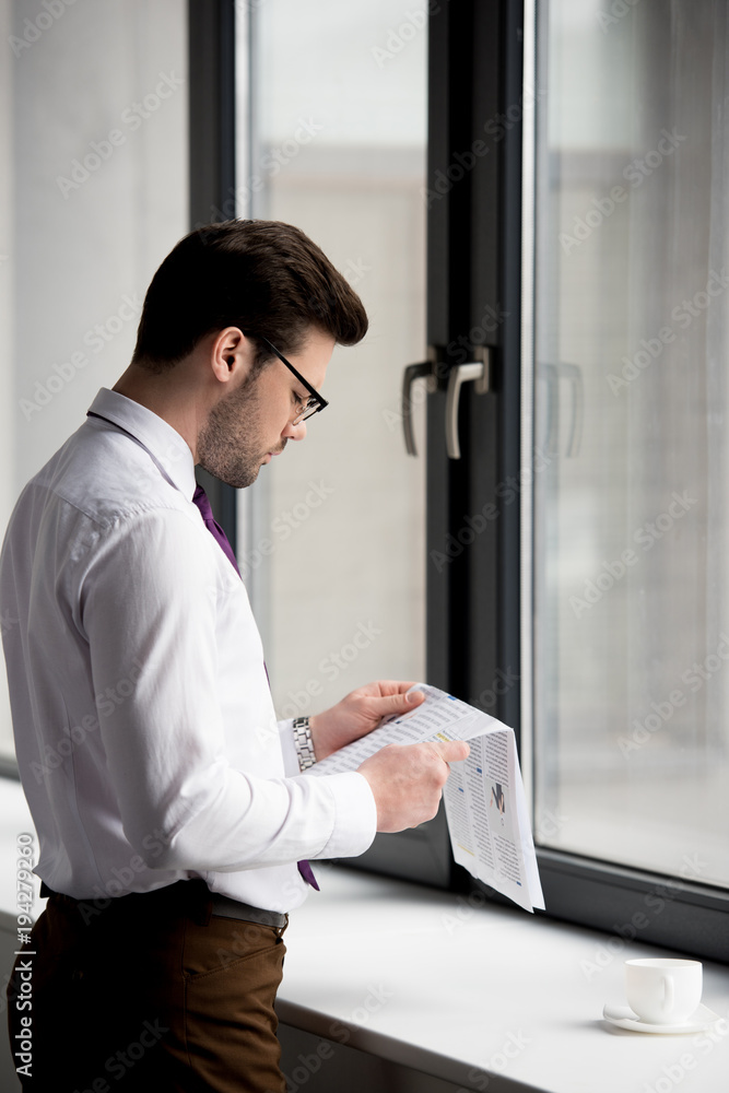 Side view of young businessman reading newspaper