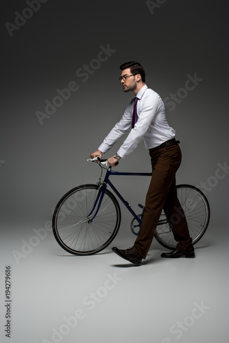 Side view of stylish businessman carrying bicycle on grey