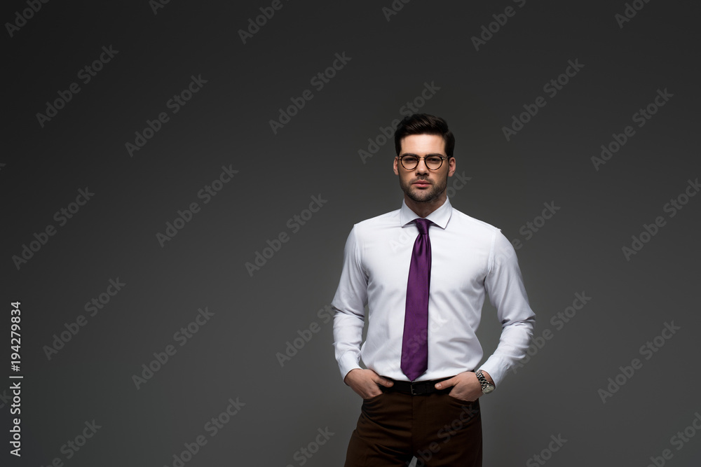 Businessman in glasses standing with fingers in pockets isolated on grey Businessman in glasses standing with fingers in pockets isolated on grey