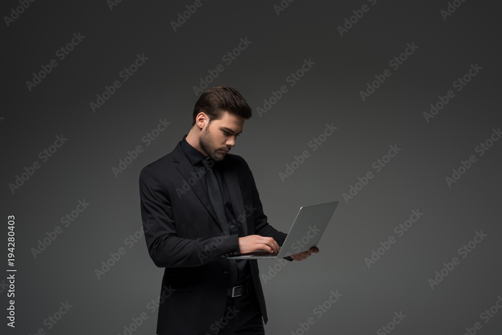 Side view of businessman typing on laptop isolated on grey Side view of businessman typing on laptop isolated on grey
