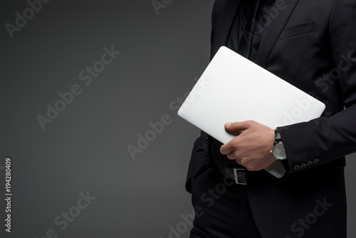 Partial view of businessman holding laptop in hand isolated on grey photo