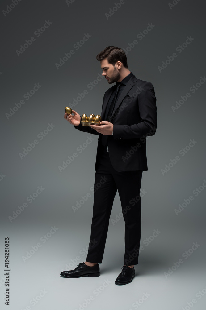 Side view of stylish male holding golden eggs on grey, easter concept Side view of stylish male holding golden eggs on grey, easter concept
