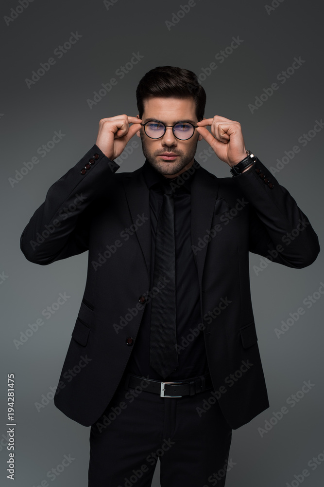 Man in stylish black suit taking off glasses isolated on grey Man in stylish black suit taking off glasses isolated on grey