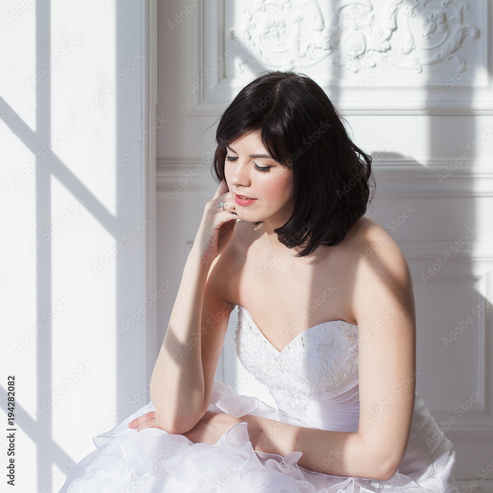 Portrait of young attractive brunette with short hair in a wedding dress. Standing at the white walls. Joyful bride. Portrait of young attractive brunette with short hair in a wedding dress. Standing at the white walls. Joyful bride.