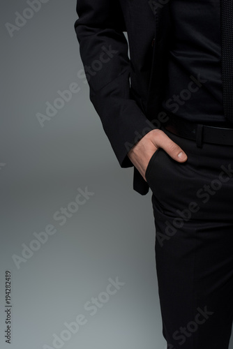 Partial view of male hand in pocket of black suit isolated on grey