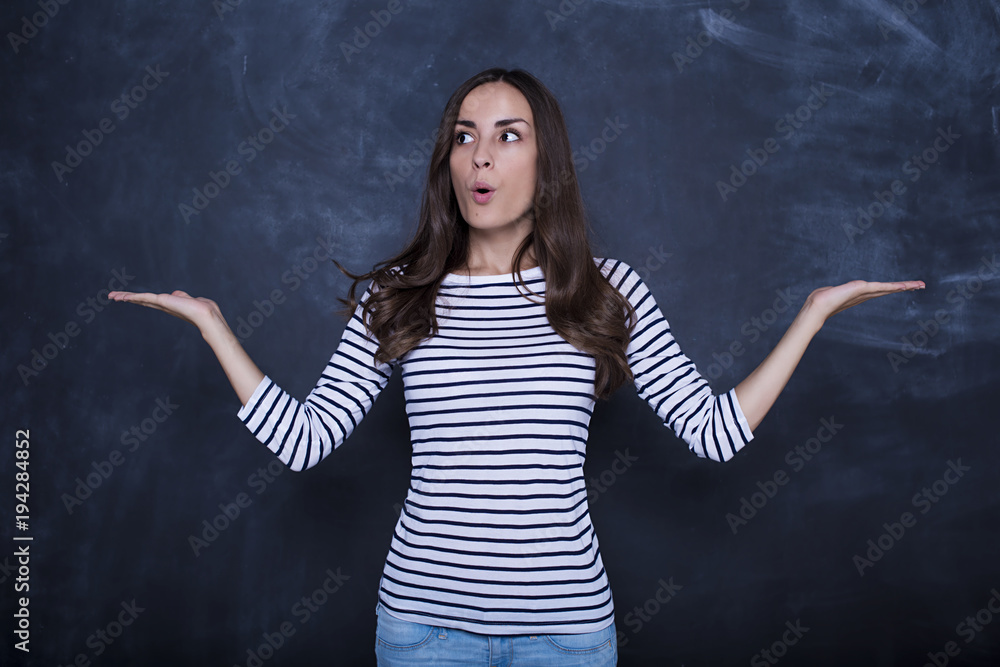Beautiful young girl is keeping hands spread showing balance and looking to the side, standing against blackboard Beautiful young girl is keeping hands spread showing balance and looking to the side, standing against blackboard