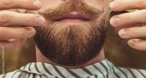 Closeup of a cropped photo of a bearded stylish men. Care beard and mustache in beauty salon. photo