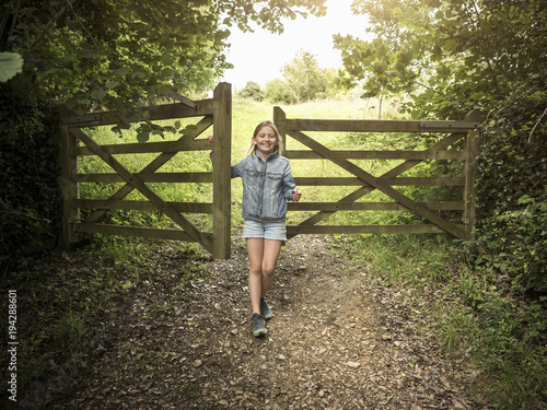 Full length of smiling girl standing by wooden gate on footpath amidst plants photo