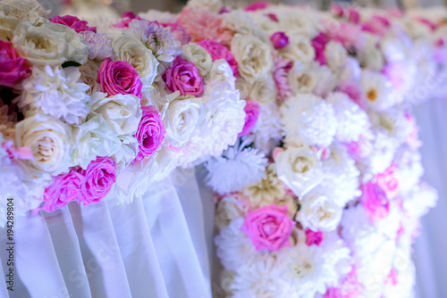 Colorful flower garlands made of white and pink roses decorate a place for wedding couple in the dinner hall