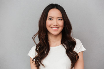 Portrait of asian lovely woman with dark curly hair posing with kind smile, isolated over gray background