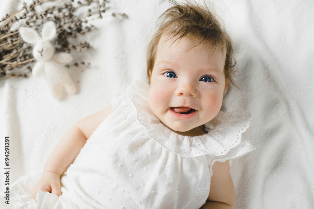 Gorgeous child in white dress lies on white bed with tiny rabbit in a bright room Gorgeous child in white dress lies on white bed with tiny rabbit in a bright room