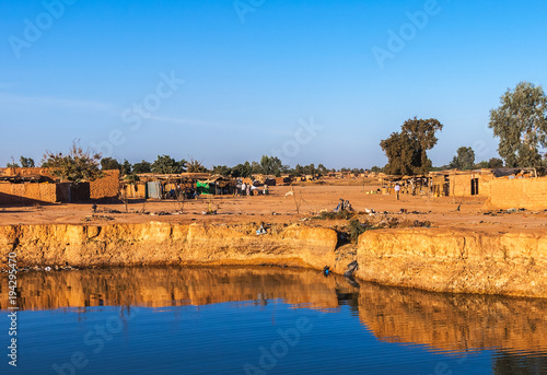 Konstfotografi Eastern township of Ouagadougou on a sunny day with a hole filled with rainwater in the foreground, Burkina Faso