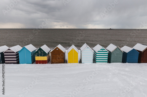 Row of beach huts in winter snow on coast of Herne Bay, Kent, England