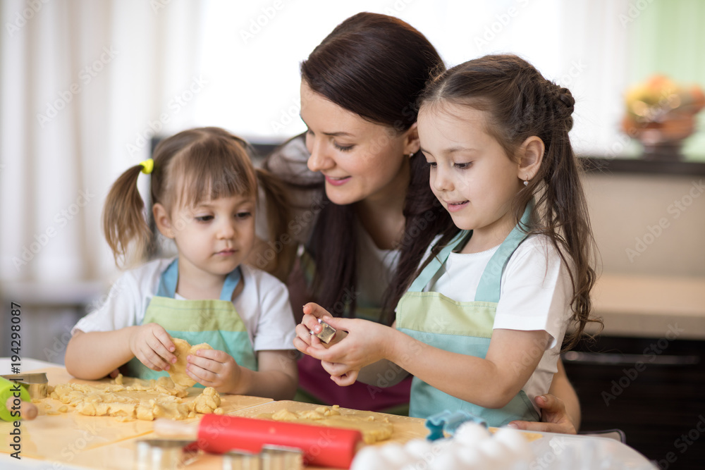 Mom with her 2 and 5 years old daughters are cooking in domestic kitchen to Mothers day Mom with her 2 and 5 years old daughters are cooking in domestic kitchen to Mothers day