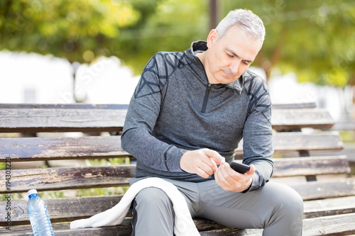 Mature man with mobile phone resting after exercising at a park