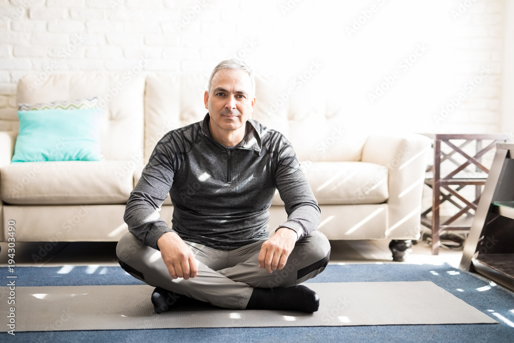 Fototapeta premium Relaxed mature man sitting on yoga mat at home