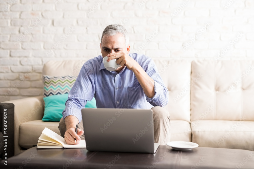 Middle aged man drinking coffee while working from home Middle aged man drinking coffee while working from home