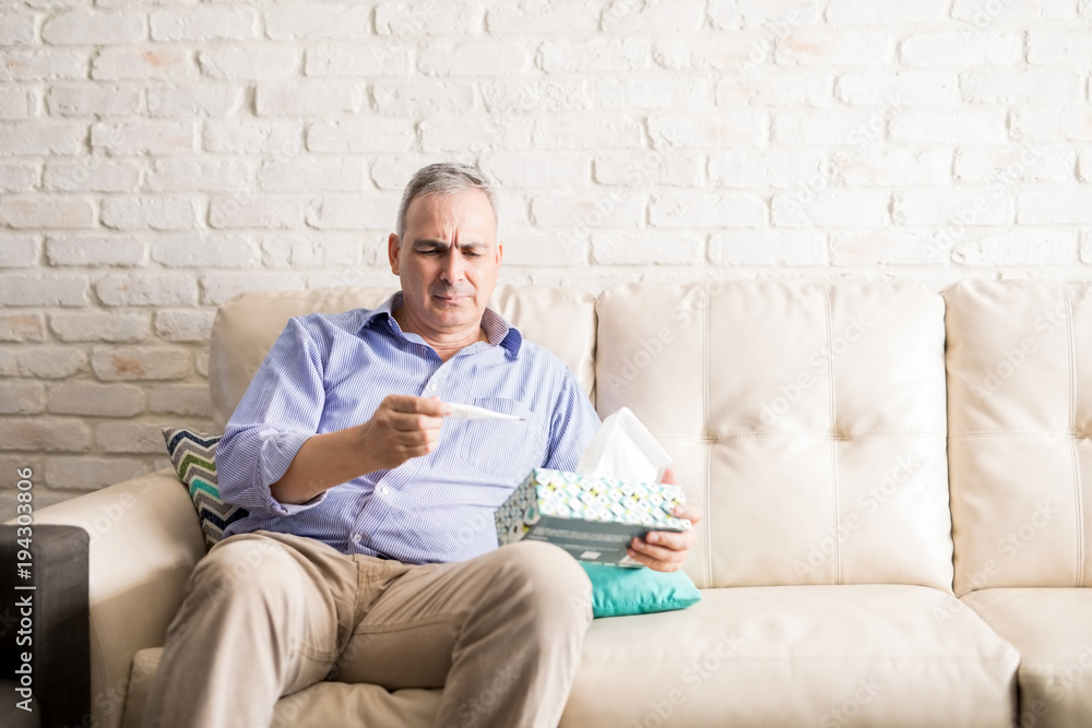 Fototapeta premium Sick man measuring his fever with thermometer
