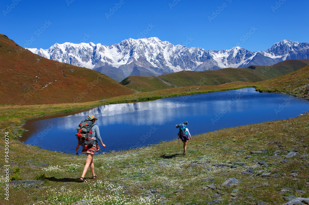 girls with large backpacks descend to picturesque lake in the mountains of Georgia
