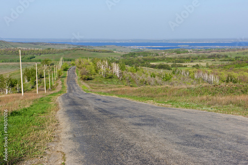 The road leads through the hills to a large river. The first spring greens and the blue sky. View from the hills to the Volga River.