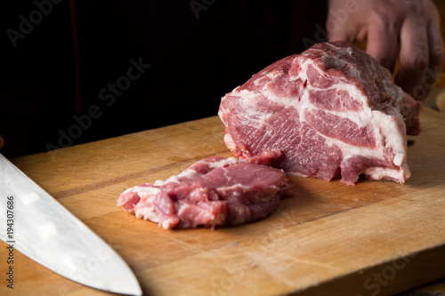 Cook cuts  fresh piece of meat on a wooden cutting board