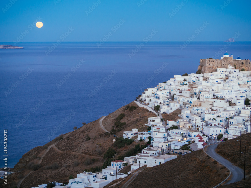 A lithe road leading to Chora of Astypalaia in blue hour and the full moon rising from the horizon