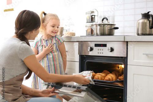 Little girl watching her mother bake croissants in oven indoors
