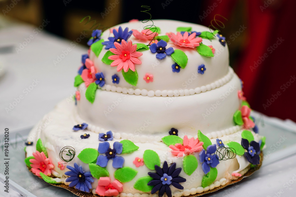 wedding cake in white sweet glaze with colorful flowers close-up on the table wedding cake in white sweet glaze with colorful flowers close-up on the table