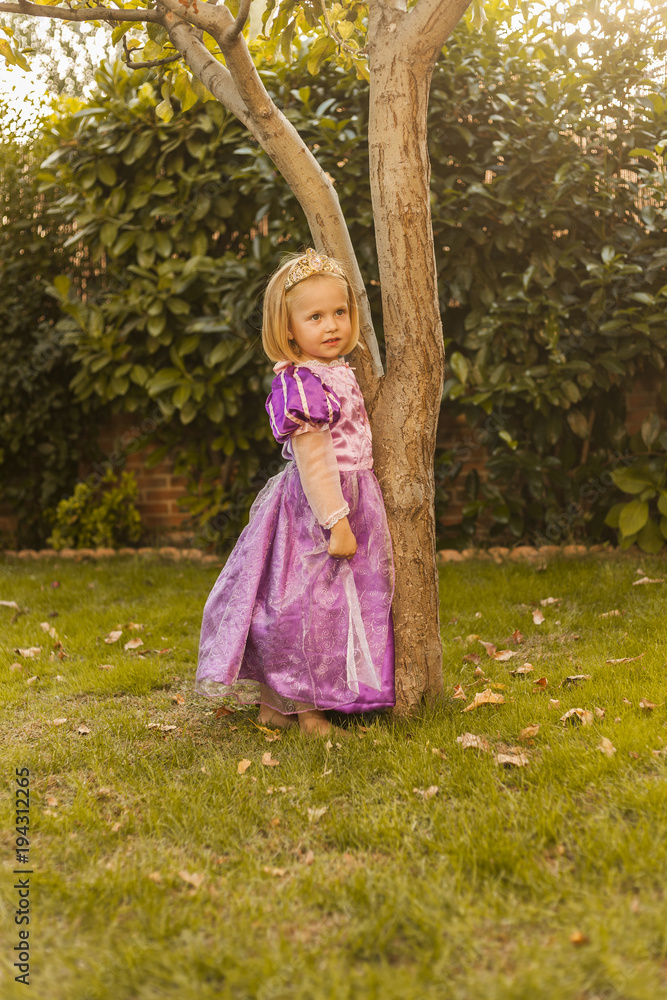 Portrait kid in a purple princess costume holding a tree. Outdoors. Sunset Portrait kid in a purple princess costume holding a tree. Outdoors. Sunset