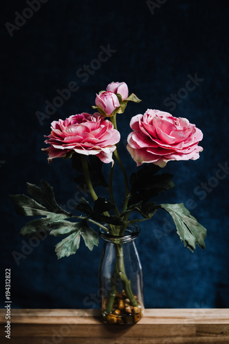 Artificial peony plant in bottle on dark background