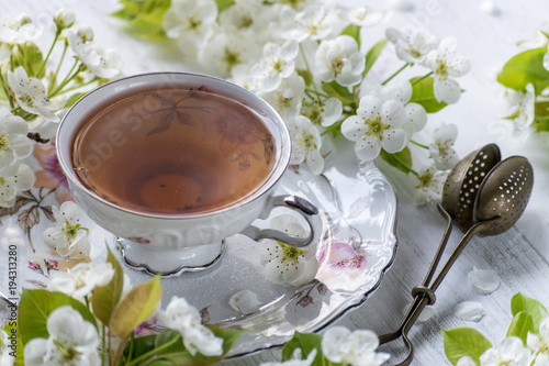Photography cup of tea in fine china surrounded by white spring flower blossoms on white tab