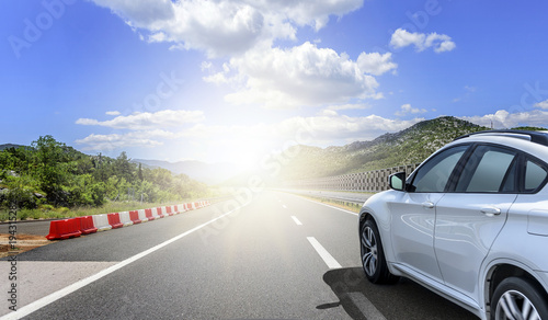 A white car rushing along a high-speed highway in the sun.