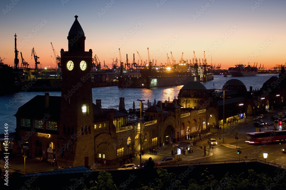 Obraz premium Silhouette of the clock tower of the famous Hamburger Landungsbruecken with commercial harbor and Elbe river, St. Pauli district, Hamburg after sunset.
