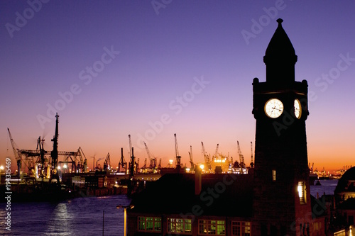Silhouettes of the Landungsbruecken clock tower and container gantry cranes in the harbour of Hamburg, Germany after sunset.