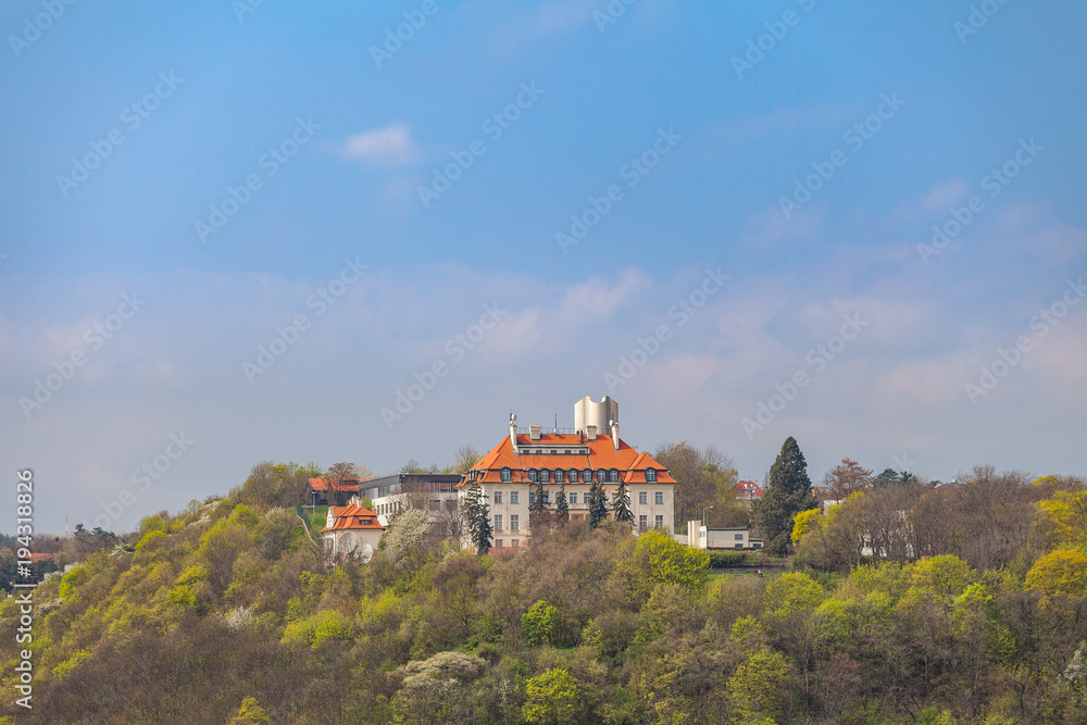 Building with red roof on a sunny hill covered by trees. Spring time.