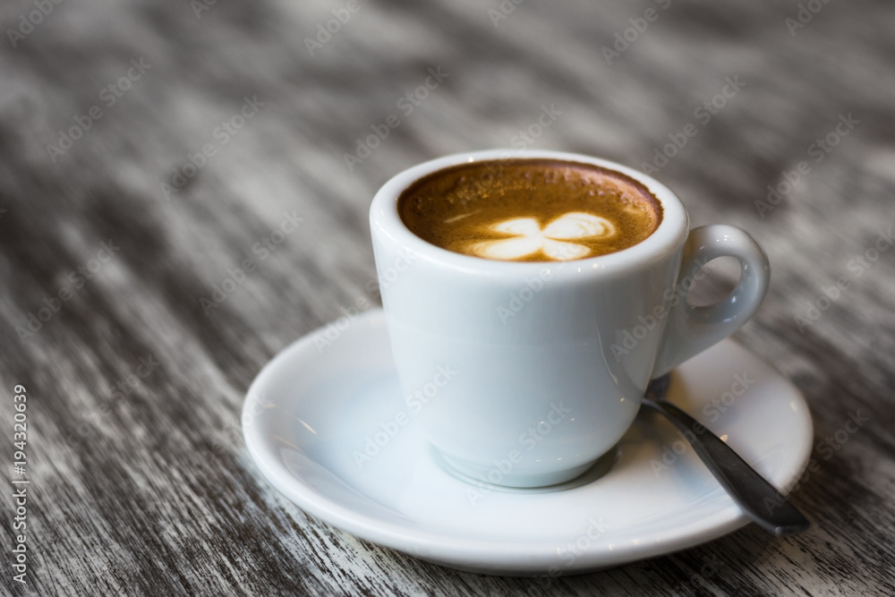White cup of coffee on plate and spoon with clover leaf shape on top. Break, meeting, leisure time concept White cup of coffee on plate and spoon with clover leaf shape on top. Break, meeting, leisure time concept