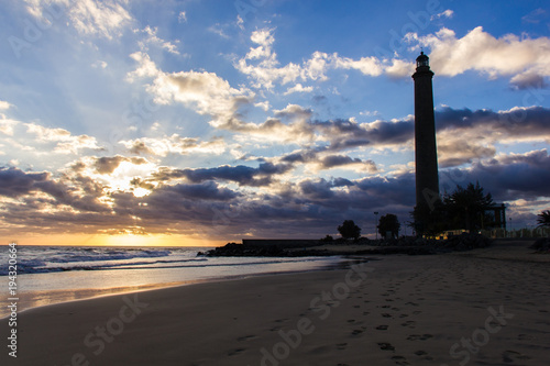 Foot prints on sand leading to Maspalomas lighthouse at splendid sunset on the beach in Canary Islands, Spain. Summer vacation, travel destination concept