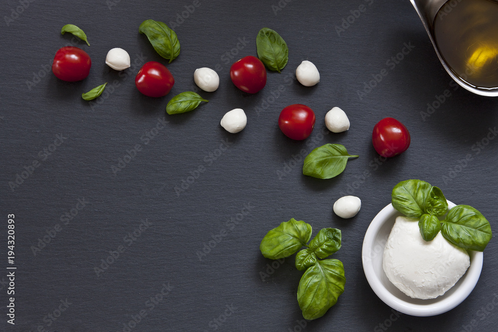 Mozzarella, olive oil, cherry tomatoes and basil on a black stone background. Top view, close-up, background, place for text. Mozzarella, olive oil, cherry tomatoes and basil on a black stone background. Top view, close-up, background, place for text.