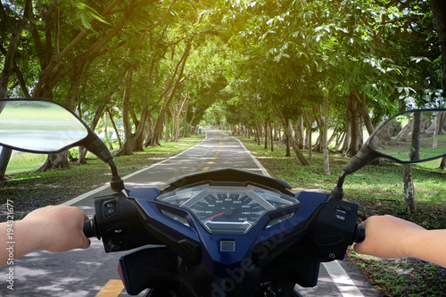 Hands of motorcyclist scooter on the road with trees