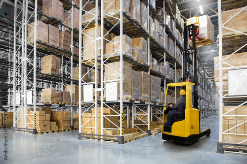 Huge distribution warehouse with high shelves and forklift with operator.