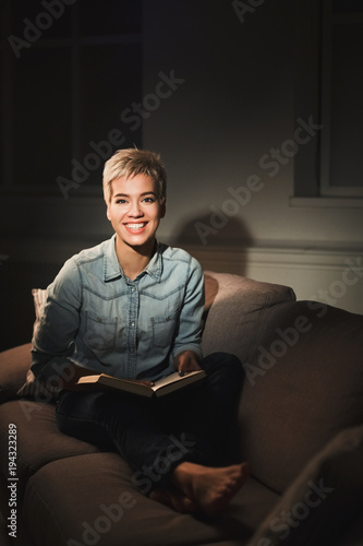 Smiling student girl reading book in dark room