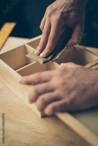 Close up cropped photo of carpenter's hands making smooth the surface on wooden casket using sandpaper he wants to sell his diy