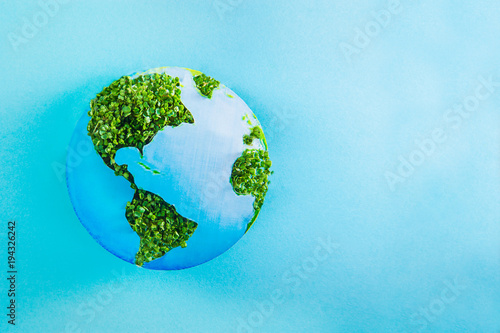 Earth model made of paper and fresh green sprouts collage on blue background. Green planet creative concept. Earth day. Selective focus, space for text.