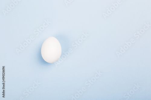 White egg on blue background. Top view, copy space