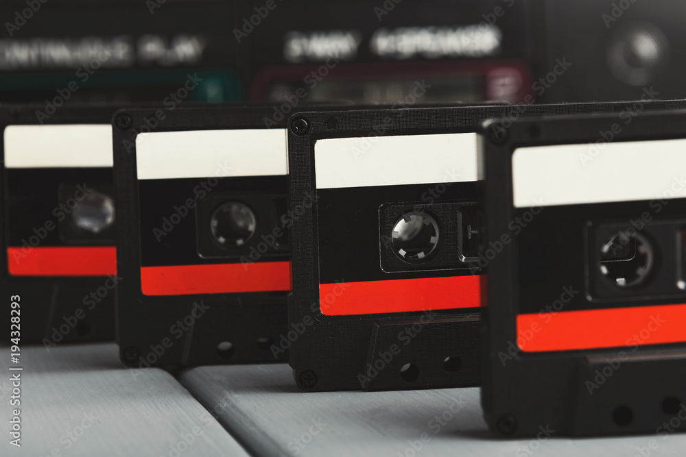 Row of vintage audio cassettes and tape recorder at gray background
