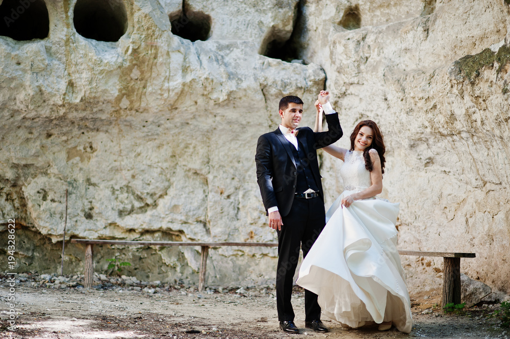 Wedding couple against cave at summer day.