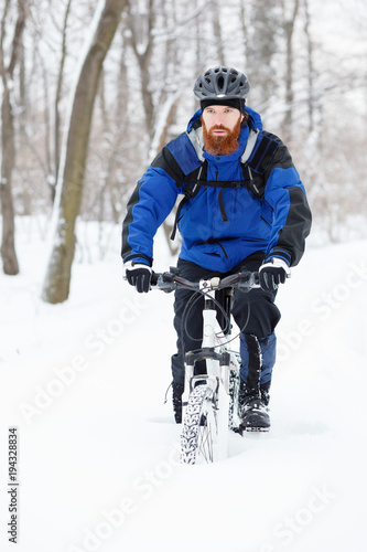 Determined male cyclist in blue jacket riding MTB toward camera through deep powder snow in a forest. Extreme sport and enduro biking concept