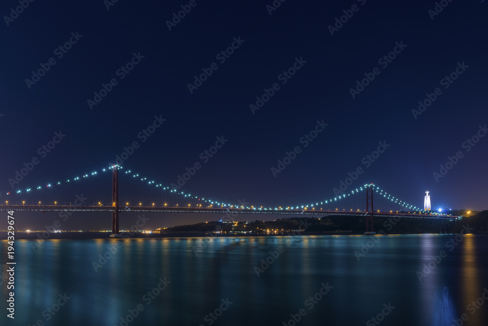 Beautiful and serene view of the Tagus River and the 25 of April Bridge (Ponte 25 de Abril) at night, in Lisbon, Portugal