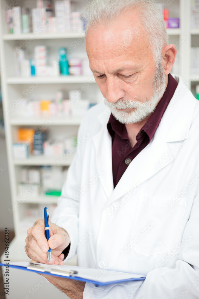 Medicine, pharmaceutics, health care and people concept - Serious senior male pharmacist with a clipboard Medicine, pharmaceutics, health care and people concept - Serious senior male pharmacist with a clipboard